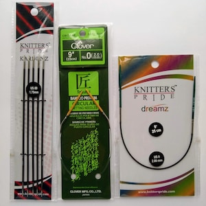 May include: Three packages of knitting needles. The first package is black and contains five knitting needles labeled "Knitter's Pride Karbonz" and "US 00 1.75mm". The second package is green and contains a 9-inch circular knitting needle labeled "Clover No. 0 (2.0 mm)". The third package is blue and contains a 9-inch circular knitting needle labeled "Knitter's Pride dreamz" and "US 0 2.00 mm".