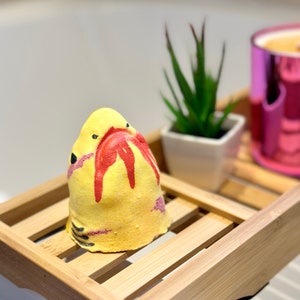 Handmade yellow shark bath bomb resting over the bathtub. The bath bomb features a cute, hand-painted shark face with vibrant yellow colour, perfect for a fun and fizzy bath time experience.