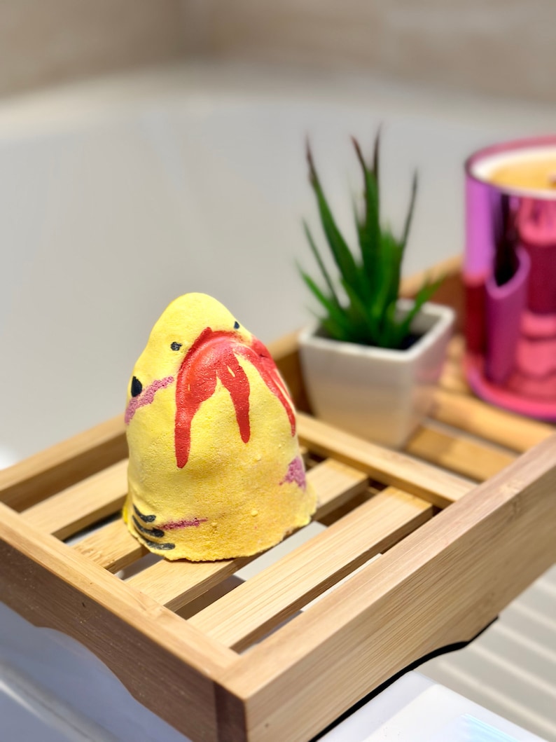 Handmade yellow shark bath bomb resting over the bathtub. The bath bomb features a cute, hand-painted shark face with vibrant yellow colour, perfect for a fun and fizzy bath time experience.