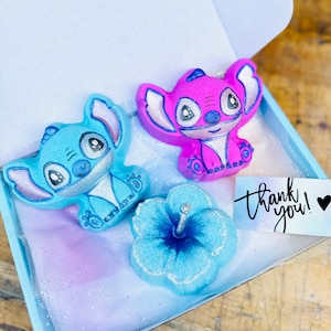 May include: A blue gift box containing a blue and pink Stitch character bath bomb, a blue hibiscus bath bomb, and a thank you card.