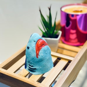Handmade blue shark bath bomb resting over the bathtub. The bath bomb features a cute, hand-painted shark face with vibrant blue colour, perfect for a fun and fizzy bath time experience.