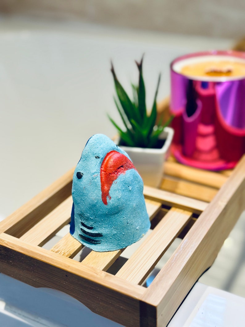 Handmade blue shark bath bomb resting over the bathtub. The bath bomb features a cute, hand-painted shark face with vibrant blue colour, perfect for a fun and fizzy bath time experience.