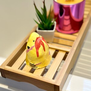 Handmade yellow shark bath bomb resting over the bathtub. The bath bomb features a cute, hand-painted shark face with vibrant yellow colour, perfect for a fun and fizzy bath time experience.