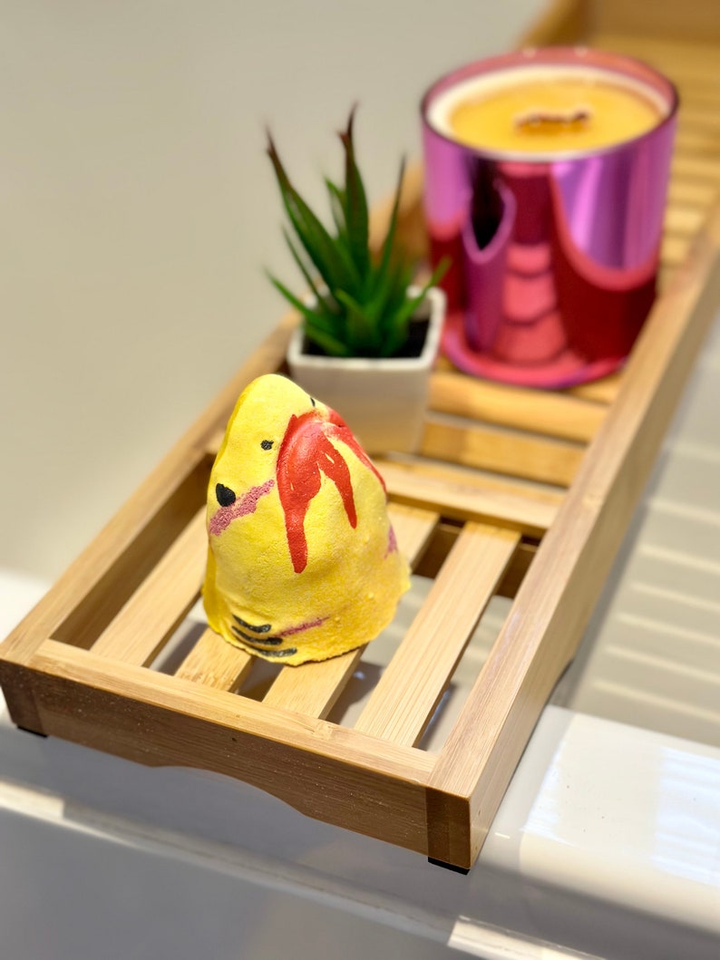 Handmade yellow shark bath bomb resting over the bathtub. The bath bomb features a cute, hand-painted shark face with vibrant yellow colour, perfect for a fun and fizzy bath time experience.