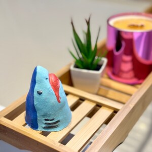 Handmade blue shark bath bomb resting over the bathtub. The bath bomb features a cute, hand-painted shark face with vibrant blue colour, perfect for a fun and fizzy bath time experience.