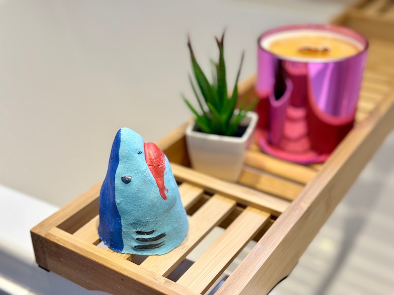 Handmade blue shark bath bomb resting over the bathtub. The bath bomb features a cute, hand-painted shark face with vibrant blue colour, perfect for a fun and fizzy bath time experience.
