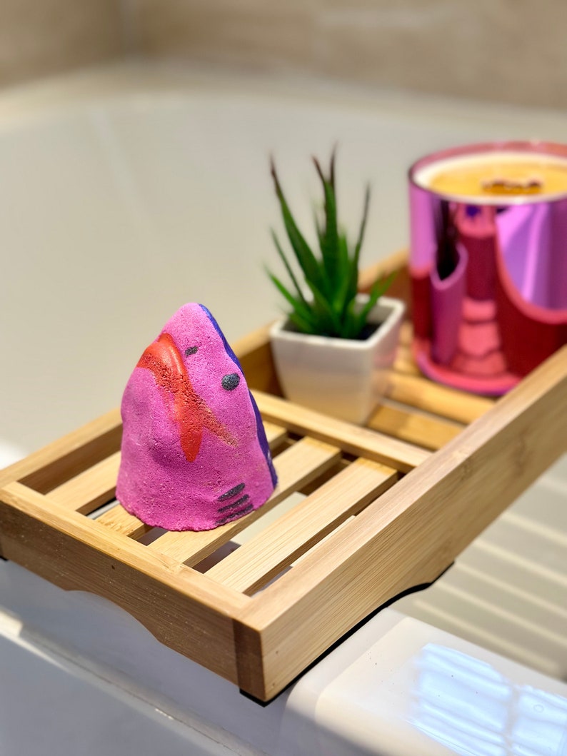 Handmade pink shark bath bomb resting over the bathtub. The bath bomb features a cute, hand-painted shark face with vibrant pink colour, perfect for a fun and fizzy bath time experience.