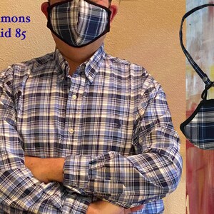 Op de afbeelding: Een blauw en wit geruit mondkapje met een zwarte rand, hangend aan een zwart koord. Het masker wordt gedragen door een persoon die een blauw en wit geruit overhemd draagt. De tekst "Simmons Plaid 85" is zichtbaar in de linkerbovenhoek van de afbeelding.