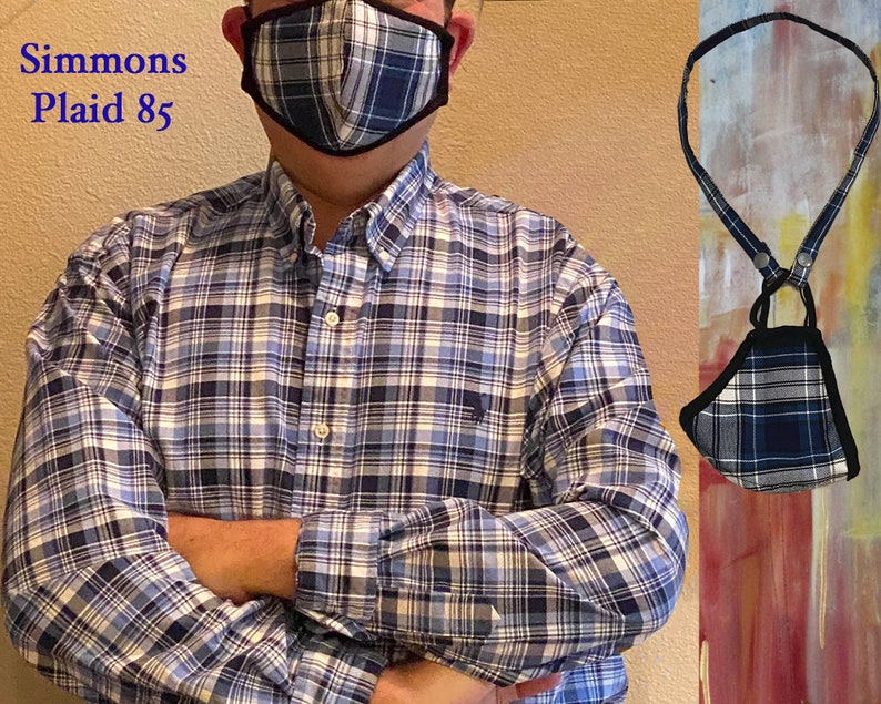 Op de afbeelding: Een blauw en wit geruit mondkapje met een zwarte rand, hangend aan een zwart koord. Het masker wordt gedragen door een persoon die een blauw en wit geruit overhemd draagt. De tekst "Simmons Plaid 85" is zichtbaar in de linkerbovenhoek van de afbeelding.