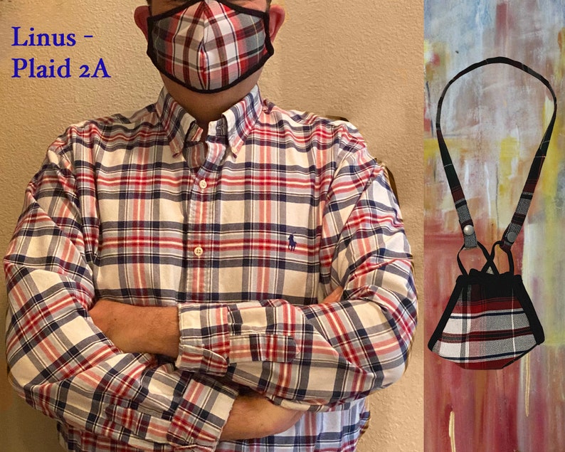 Op de afbeelding: Een rood, wit en zwart geruit mondkapje met een zwart koord. Het mondkapje hangt om de nek van de persoon die het draagt. De tekst "Linus - Plaid 2A" is zichtbaar in de afbeelding.