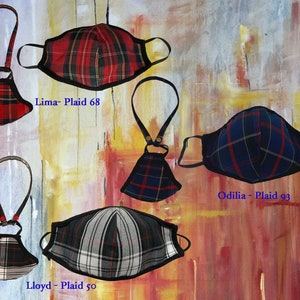 Op de afbeelding: Vier geruite mondkapjes met zwarte bies en verstelbare bandjes. De mondkapjes zijn in verschillende kleuren en patronen, waaronder rood, blauw en zwart. De tekst "Lima - Plaid 68", "Odilia - Plaid 93" en "Lloyd - Plaid 50" is zichtbaar op de afbeelding.