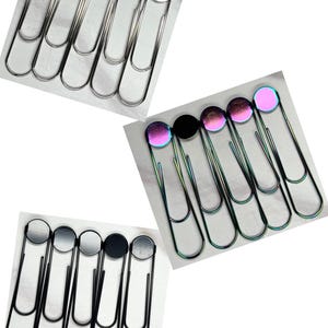 May include: Three sets of oversized paper clips. One set has silver clips with silver tops, another has black clips with silver and black tops, and the last set has iridescent clips with iridescent and black tops.