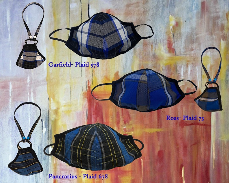 Op de afbeelding: Vier verschillende geruite mondmaskers met zwarte elastieken en een bijpassend geruit koord. De maskers zijn blauw, zwart en wit met verschillende ruitpatronen. De koorden zijn met een kleine metalen ring aan de maskers bevestigd. De maskers zijn gelabeld met "Garfield - Plaid 578", "Ross - Plaid 73" en "Pancratius - Plaid 678".