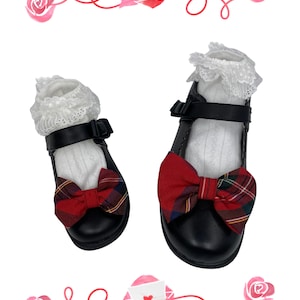 May include: A pair of black shoes with red and black plaid bows, white lace trim, and white socks. The shoes are on a white background with pink roses and hearts.
