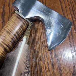 May include: A small, silver axe with a wooden handle and a brown and white feather tied to the handle.