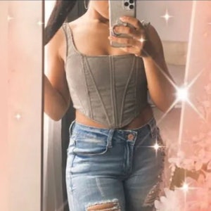 以下が含まれることがあります： 尖った裾のグレーのデニムコルセットトップ。トップはスクエアネックで、ウエストがシェイプされています。