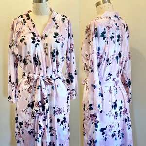 May include: A pink floral robe with long sleeves and a tie belt. The robe has a V-neck and a floral print with pink, white, and green flowers.