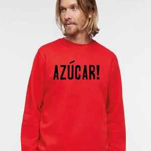 May include: A red sweatshirt with the text "AZ&Uacute;CAR!" printed in black on the front.