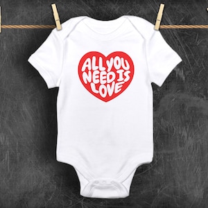May include: White baby onesie with a red heart graphic that says "All you need is love" in white letters.