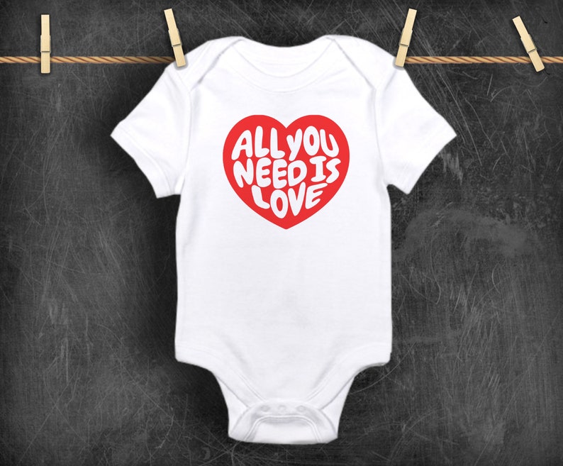 May include: White baby onesie with a red heart graphic that says "All you need is love" in white letters.