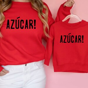 May include: Red matching sweatshirts with the Spanish phrase "Az&uacute;car!" printed in black on the front.