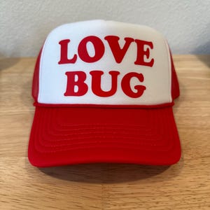 May include: A red and white trucker hat with the words "LOVE BUG" in red letters on the front.