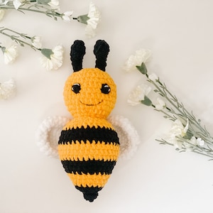 May include: A crocheted bee toy with black and yellow stripes, white wings, and a smiling face.