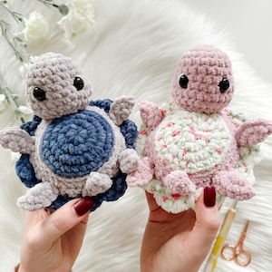 May include: Two crocheted turtle toys. One is blue and gray, the other is pink and white with a floral pattern.