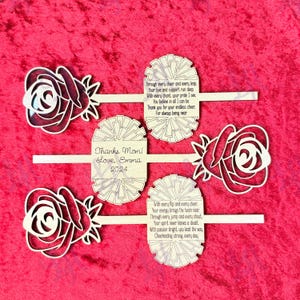 May include: A set of three wooden cheerleading sticks with a rose design and a pom-pom. The sticks have a message that says "Thanks Mom! Love, Emma 2024" and "Through every cheer and every leap, your love and support run deep. With every chant, your pride I see. You believe in all I can be. Thank you for your endless cheer. For always being near." and "With every flip and every cheer. Your energy brings the team near. Through every jump and every shout, your spirit never leaves a doubt. With passion bright, you lead the way. Cheerleading strong, every day."