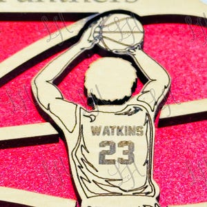 May include: Wooden basketball ornament featuring a player in a jersey with "Watkins" and the number "23". The player is holding a basketball above their head, set against a red background. The word "Panthers" is at the top.