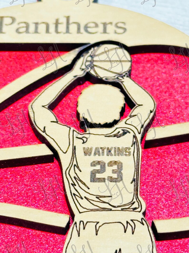 May include: Wooden basketball ornament featuring a player in a jersey with "Watkins" and the number "23". The player is holding a basketball above their head, set against a red background. The word "Panthers" is at the top.