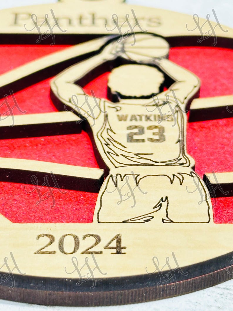 May include: Wooden basketball ornament featuring a player in a jersey with the name "Watkins" and the number "23". The ornament has a red background and the year "2024" engraved at the bottom. The word "Panthers" is at the top.