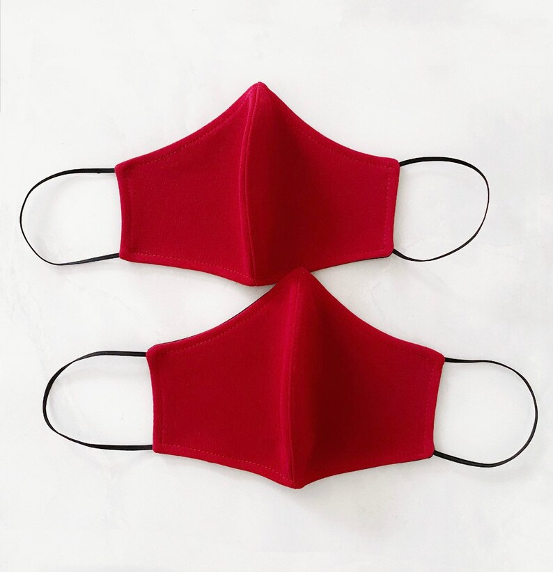 Pode incluir: Duas m&aacute;scaras de tecido vermelho com la&ccedil;os el&aacute;sticos pretos para as orelhas.