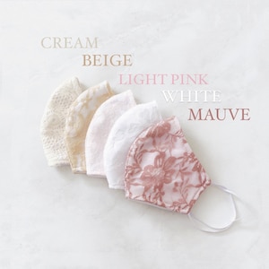 Könnte beinhalten: Fünf Gesichtsmasken aus Spitze in verschiedenen Farben: Creme, Beige, Hellrosa, Weiß und Mauve. Die Masken sind in einer Reihe angeordnet, wobei die Crememaske oben und die Mauvemaske unten liegt.