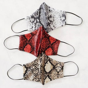 May include: Three face masks with a snake skin pattern. The masks are red, black and white, and beige. The masks have elastic ear loops.