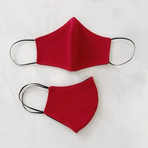 May include: Two red fabric face masks with black elastic ear loops. The masks are made of a soft, breathable material.