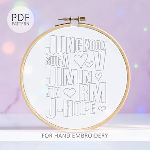May include: A round embroidery hoop with a white fabric featuring the names Jungkook, Suga, V, Jimin, Jin, RM, and J-Hope in black, with heart symbols. The text "PDF PATTERN" is at the top left, and "FOR HAND EMBROIDERY" is at the bottom.