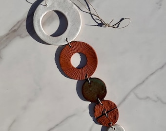 May include: A white, brown, and green ceramic mobile with six circular pieces hanging from a string. The top piece is white with a speckled finish and a hole in the center. The other pieces are various shades of brown and green with textured surfaces.