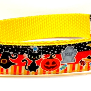 May include: Yellow Halloween-themed dog collar with a black and orange patterned ribbon. The ribbon features Halloween icons like ghosts, pumpkins, and witch hats. The collar has a yellow plastic buckle and a metal D-ring.