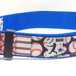 May include: A blue dog collar with a baseball-themed pattern featuring red, white, and blue baseballs, a baseball player, and the word "BASE" on a blue background.