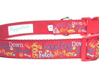 May include: Red dog collar with a plastic buckle and metal ring. The collar features the text "Good Dog", "Fetch", "Stay", "Speak", and other commands in colorful lettering. The brand name "PupperStuff" is also visible.