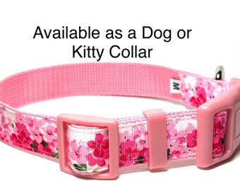 May include: Pink dog or kitty collar with a floral pattern. The collar features a pink buckle and a silver metal loop. The text "Available as a Dog or Kitty Collar" is visible.
