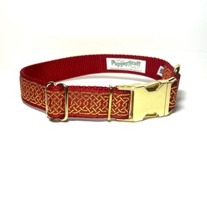 May include: Red dog collar with a gold Celtic knot design and a gold-colored buckle. The collar has the text "PupperStuff" printed on it. The collar is made of a durable material.
