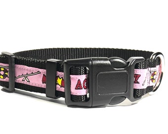 May include: A pink and black dog collar with a black buckle and a silver ring. The collar has a pink ribbon with a red and yellow design and the text "ACME" on it.