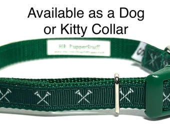 May include: A green dog or kitty collar with a white crossed-hammer pattern. The collar has a green plastic buckle and a metal slider. The text "Available as a Dog or Kitty Collar" is at the top.