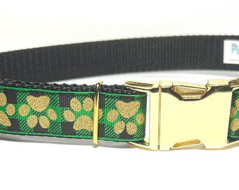May include: Black dog collar with a gold buckle. The collar features a green and black plaid pattern with gold paw prints. The collar has a gold metal buckle and a black nylon strap.