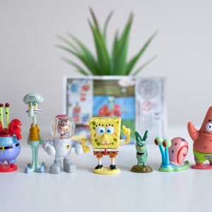 Può includere: Un set di sette figurine di plastica colorate di personaggi del cartone animato SpongeBob. I personaggi includono SpongeBob, Patrick Stella, Squidward Tentacoli, Sandy Cheeks, Plankton, Gary il Lumacone e Mr. Krabs.