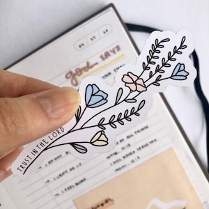 May include: A white sticker with a floral design and the text "TRUST IN THE LORD". The flowers are blue, pink, and yellow.