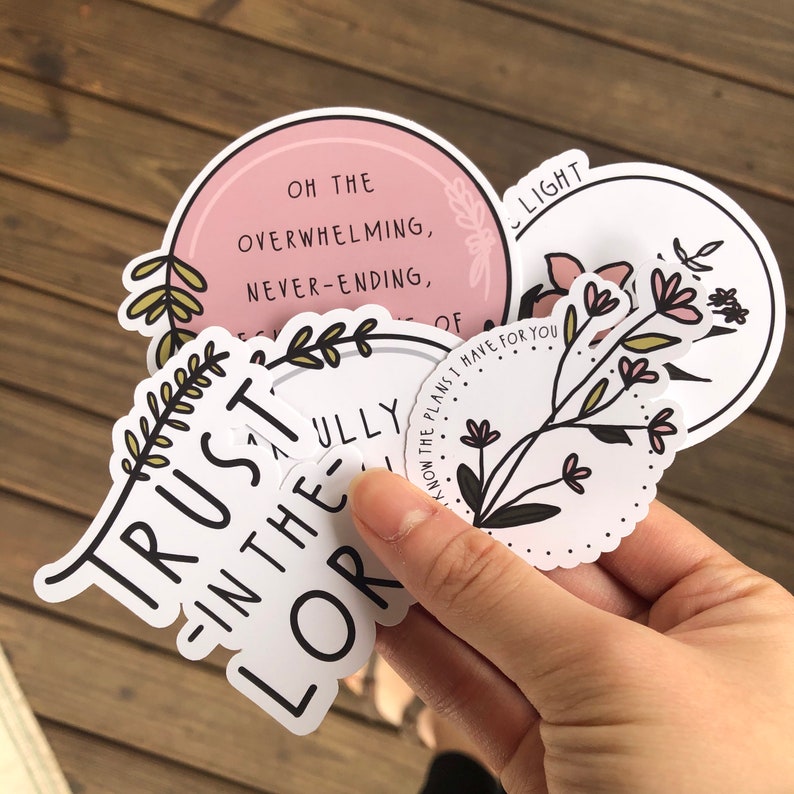 May include: A set of five round stickers with inspirational quotes and floral designs. The stickers feature phrases like "Trust in the Lord" and "Oh the overwhelming, never-ending..."  The stickers are white with black text and floral illustrations.