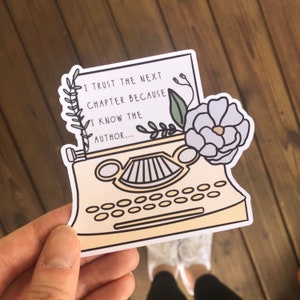 May include: A yellow typewriter with a white paper page that reads "I trust the next chapter because I know the author..." with a floral design on the top of the typewriter.